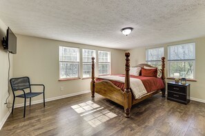 A bedroom with a wooden four-poster bed, a nightstand, a chair, and large windows.