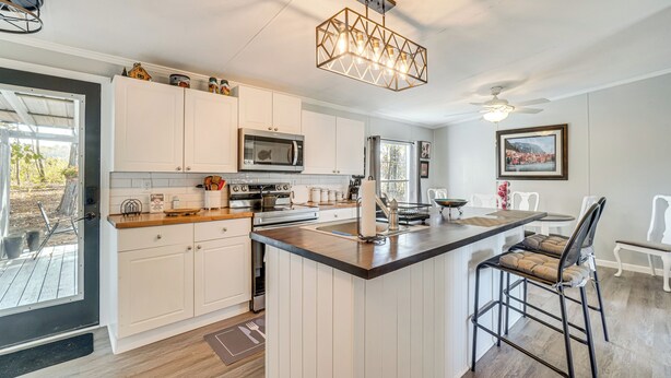 A modern kitchen with white cabinets, a central island, and a dining area with a table and chairs. - Relax Fireside! Retreat Near Chickamauga Lake (Decatur)
