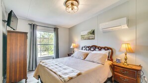 A bedroom with a bed, bedside lamps, a wooden wardrobe, a window with curtains, and an air conditioning unit. - Relax Fireside! Retreat Near Chickamauga Lake (Decatur)
