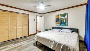 Een slaapkamer met een bed, een plafondventilator, een schilderij en een garderobe.