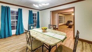 Een eetruimte met een tafel gedekt voor vier personen, een schaal fruit en een uitzicht op een woonkamer door een open deur.
