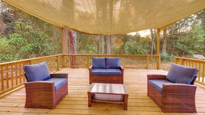 Een overdekt terras met rieten meubels en een tafel, omringd door een houten balustrade en bomen.