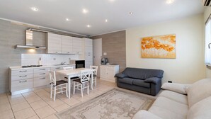 A modern kitchen with white cabinets, a dining table with chairs, a gray sofa, and a decorative painting on the wall.
