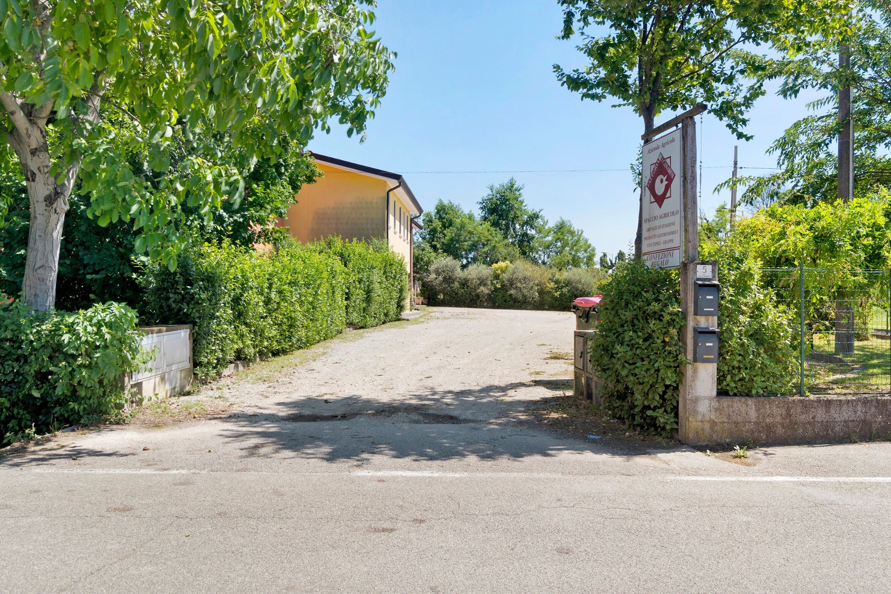 Une allée pavée mène à un bâtiment à la façade jaune, entouré de verdure et agrémenté d’une enseigne.
