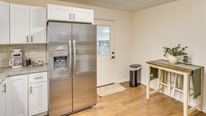 A kitchen with white cabinets, a stainless steel refrigerator, a coffee maker, and a trash can.