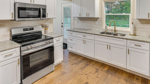 A modern kitchen with white cabinetry, stainless steel appliances, and a window with a view of greenery.