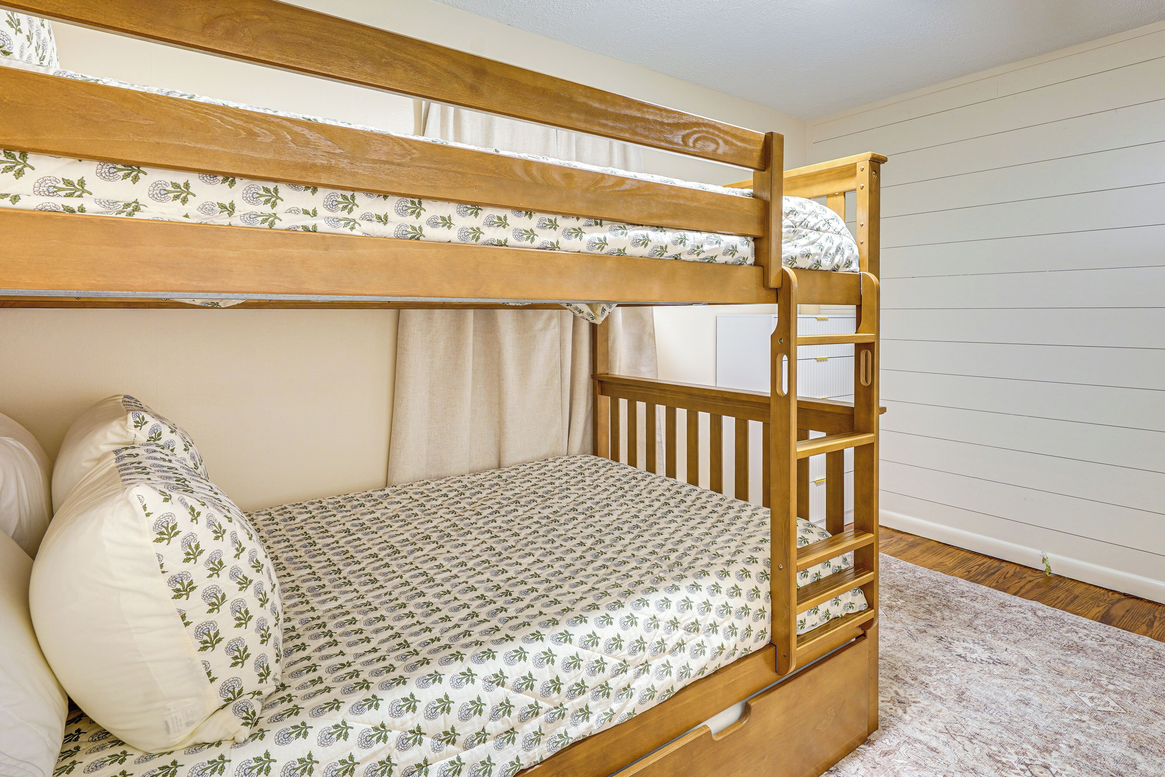 Una cama litera con colcha estampada, cabecera de madera y pared blanca con líneas horizontales.