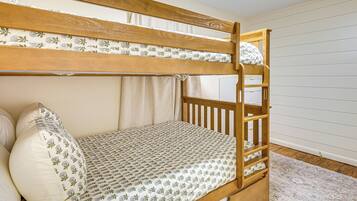 Una cama litera con colcha estampada, cabecera de madera y pared blanca con líneas horizontales.