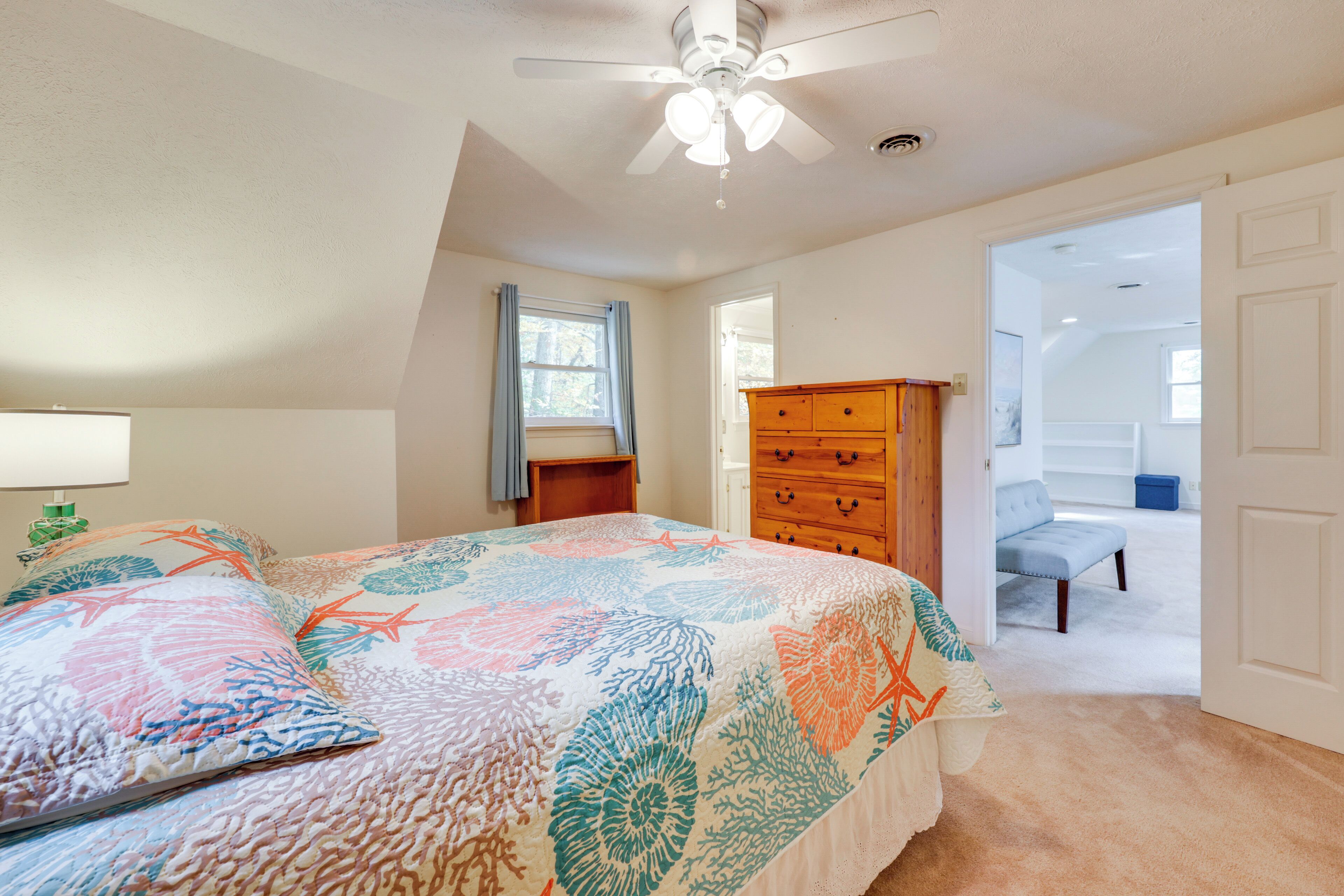 Un dormitorio con cama, cómoda, ventilador de techo y vista a otra habitación.
