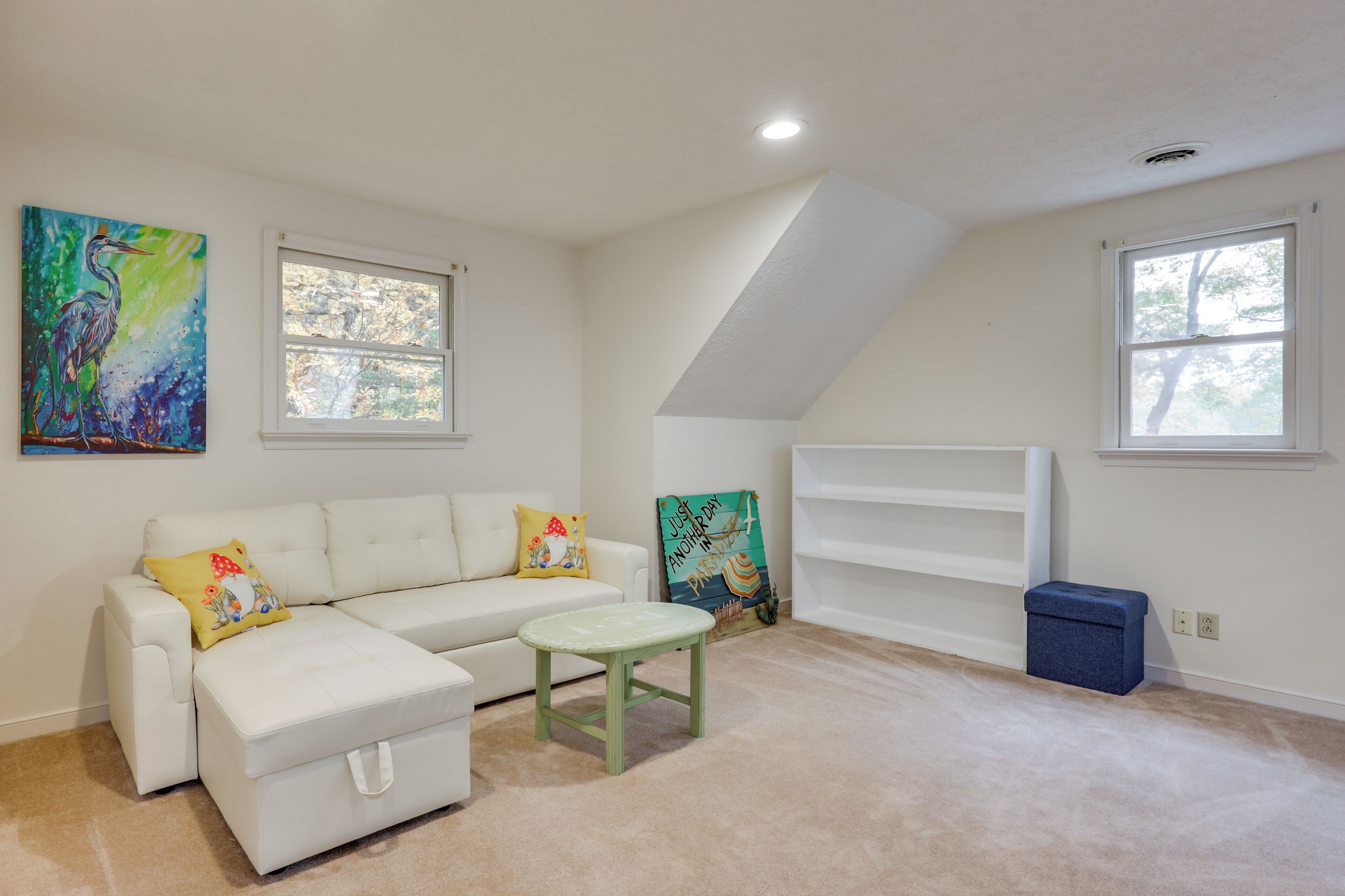A room with a white sofa, a small green stool, and two paintings on the wall.