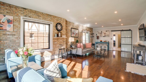 A spacious living area with a brick wall, a large window, and a modern kitchen in the background. - Pet Friendly! Near Casinos & Lake Michigan Beaches (Hammond)