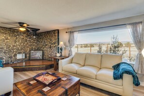A living room with a stone wall, a beige sofa, a wooden coffee table, and a view of the outdoors. - 7 Mi to Dakota Hot Springs: Penrose Group Getaway! (Penrose)
