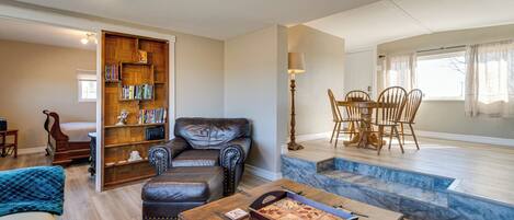 A living room with a leather sofa, a wooden coffee table, a bookshelf, and a dining area with a table and chairs.