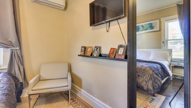 A bedroom with a bed, a chair, a TV mounted on the wall, and a shelf with books and decorations. - Easy Commute to Newark & Nyc! Extended Stay Unit (Irvington)