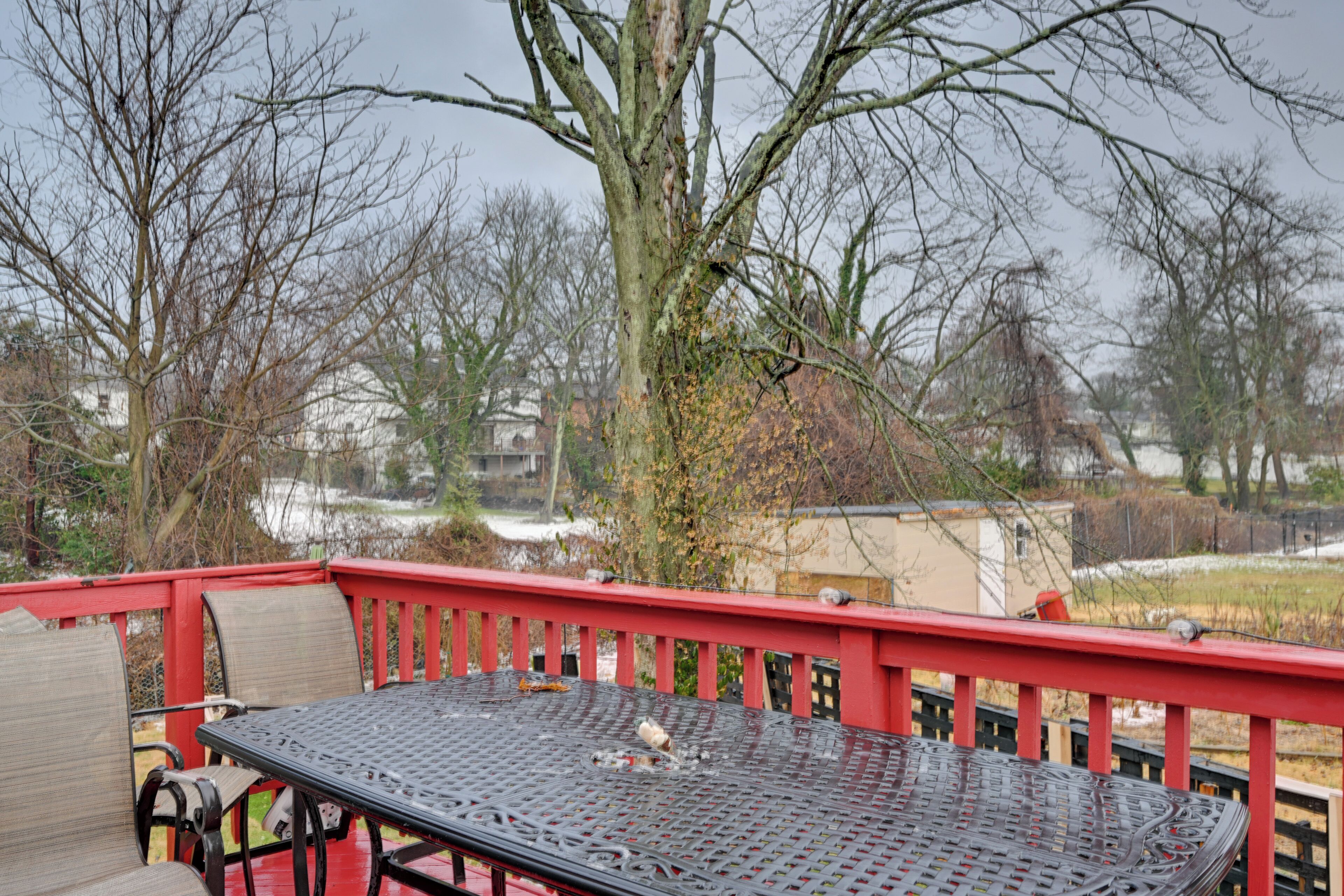 Una mesa metálica con sillas sobre una terraza roja, rodeada de árboles sin hojas y un paisaje nevado.