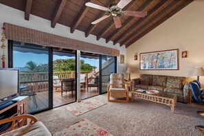 A spacious living area with a ceiling fan, a sofa, a chair, and a television. - Maui Kamaole H-208 – Oceanview Poolside Condo Close to Beaches and Dining (Kihei)