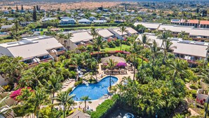 A resort with a swimming pool surrounded by palm trees and a view of distant hills. - Maui Kamaole H-208 – Oceanview Poolside Condo Close to Beaches and Dining (Kihei)