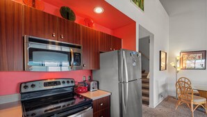 A modern kitchen with stainless steel appliances, wooden cabinets, and a red accent wall. - Maui Kamaole H-208 – Oceanview Poolside Condo Close to Beaches and Dining (Kihei)