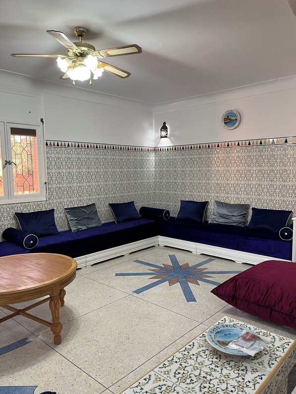 A living room with a sofa set, a wooden table, patterned tiles, and a ceiling fan.