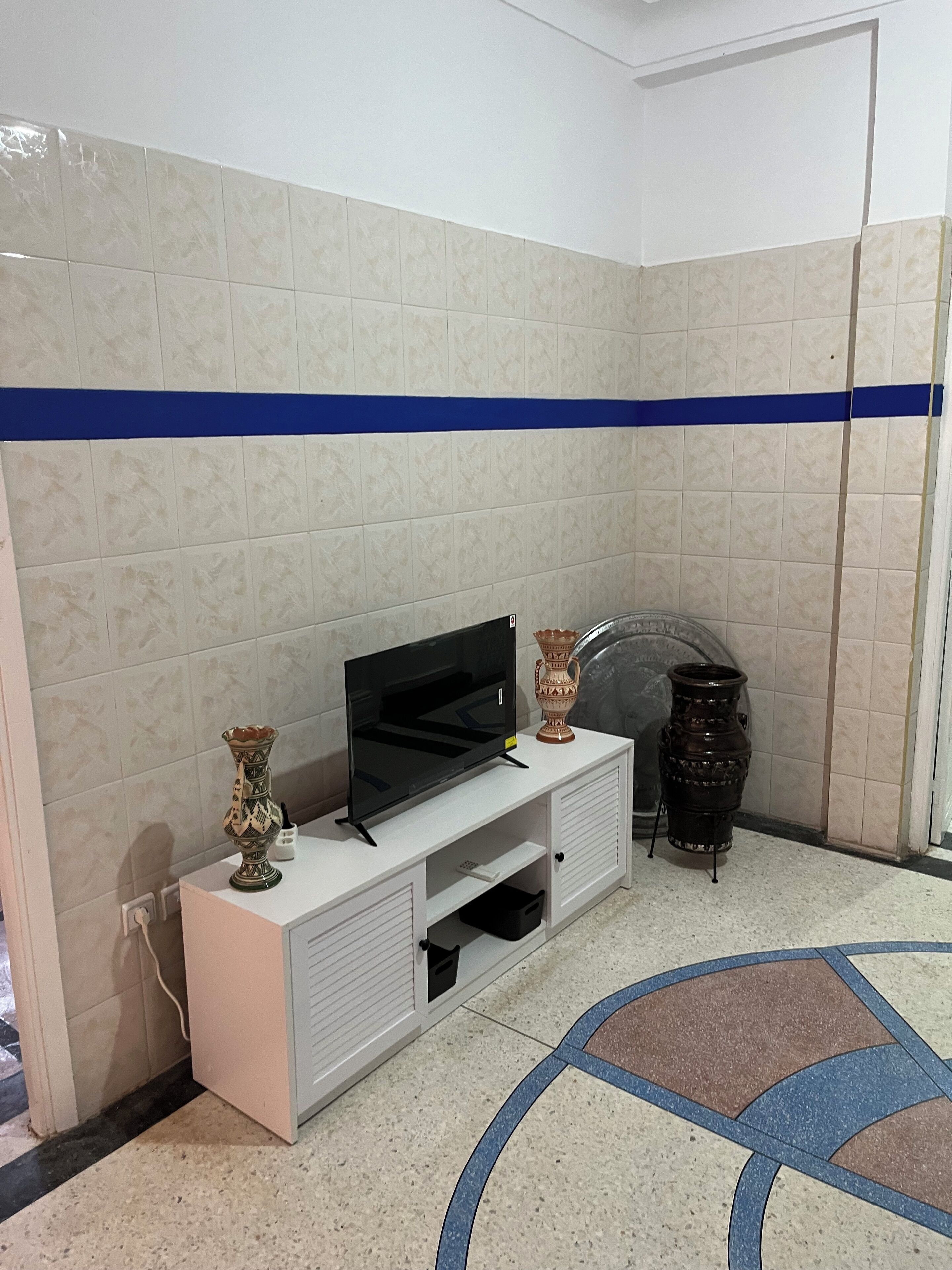 A corner room with a TV on a white cabinet, a decorative vase, and a black speaker.