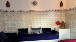 A room with a blue sofa, a red cushion, a decorative rug, and a wall with patterned tiles. - VILLA HARYOULI with its mythical Haouzia Beach and Medina of painters (Azemmour)