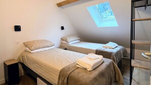 Ett sovrum med två sängar, synliga träbjälkar, ett takfönster och en inbyggd hylla.