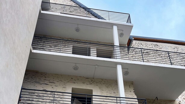 Un immeuble à plusieurs étages, doté de balcons, avec une fenêtre visible au rez-de-chaussée et une façade en pierre.