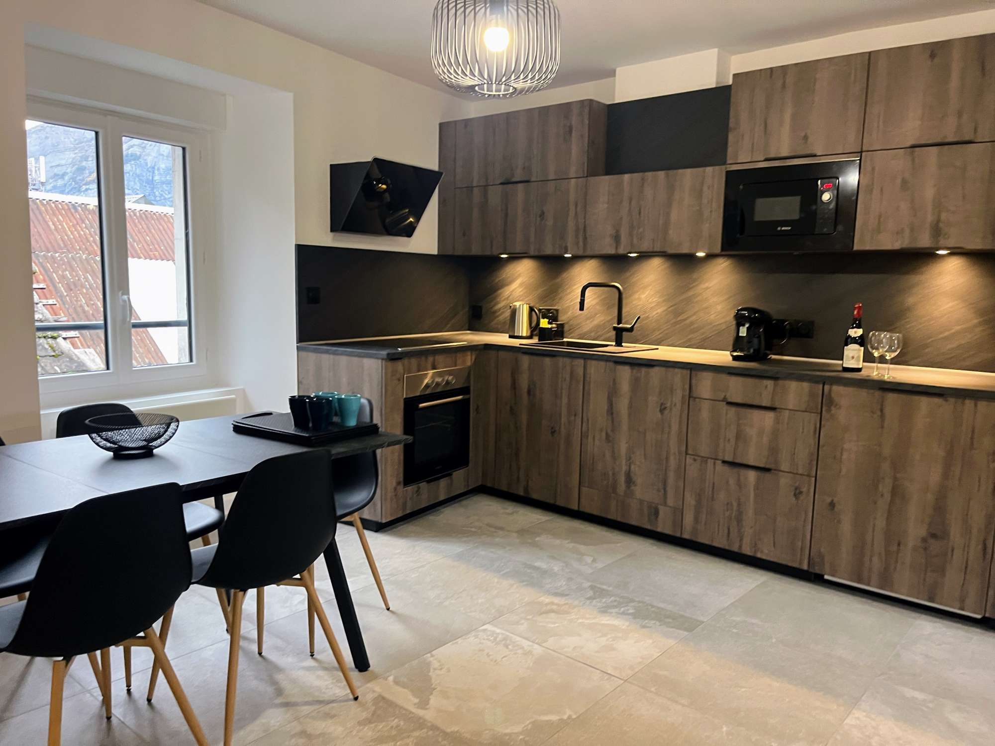 Una cocina moderna con armarios de madera, horno empotrado, microondas y una zona de comedor con mesa y sillas.