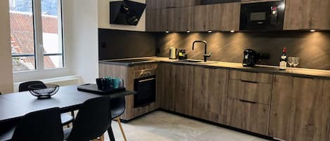 A modern kitchen with wooden cabinets, a built-in oven, a microwave, and a dining area with a table and chairs.