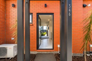 A building entrance with a brick facade, a glass door, and a visible interior hallway. - Cozy Central Loft | Walk to CBD & Stadium (Christchurch)