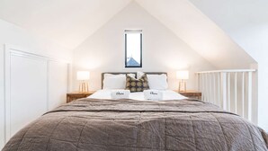 A bedroom with a sloped ceiling, a bed with a brown quilt, two bedside lamps, and a framed picture above the bed. - Cozy Central Loft | Walk to CBD & Stadium (Christchurch)