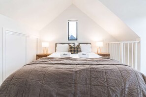 A bedroom with a sloped ceiling, a bed with a brown quilt, two bedside lamps, and a framed picture above the bed. - Cozy Central Loft | Walk to CBD & Stadium (Christchurch)