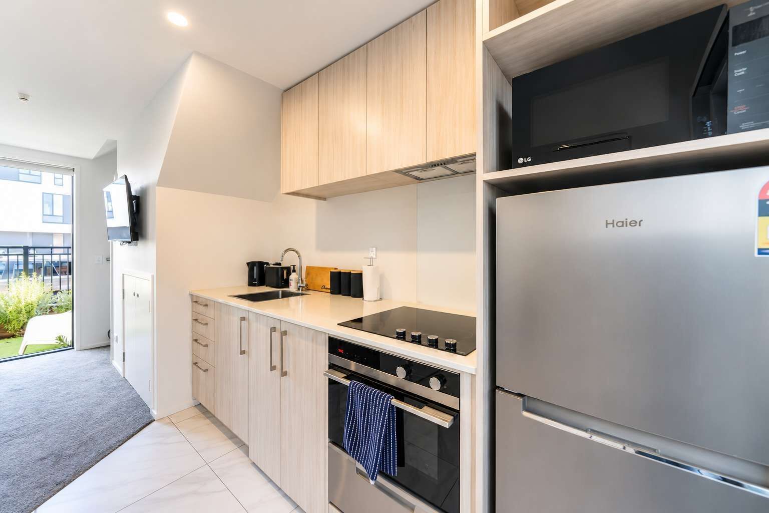 Una cocina moderna con un refrigerador de acero inoxidable, un horno empotrado y una cocina vitrocerámica negra.