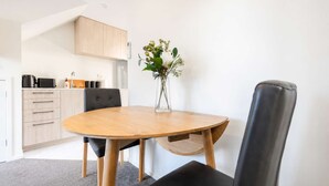 A modern kitchen with wooden cabinets, a round dining table, and a vase with flowers. - Cozy Central Loft | Walk to CBD & Stadium (Christchurch)