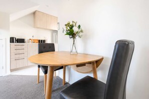 A modern kitchen with wooden cabinets, a round dining table, and a vase with flowers. - Cozy Central Loft | Walk to CBD & Stadium (Christchurch)