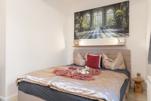 Ein Schlafzimmer mit einem großen Bett, einem Gemälde darüber und einem kleinen Holfnachtkästchen.