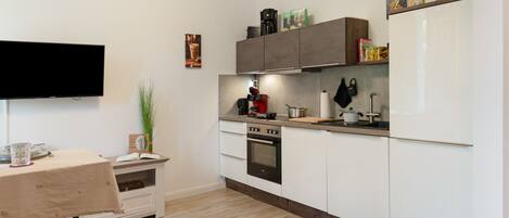 Una cocina moderna con armarios blancos, horno empotrado y cafetera.