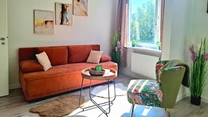 Een woonkamer met een bank, een klein rond tafeltje, een stoel en een raam met uitzicht op groen.