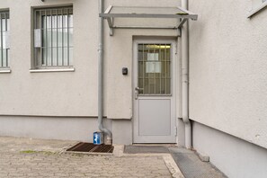 Entrada de un edificio con una puerta gris, un escalón pequeño y una rejilla metálica.