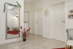 Ein Zimmer mit einem großen Spiegel, einer Tür mit einer verzierten Platte, einem kleinen Tisch mit einer Pflanze und einem roten Teppich.