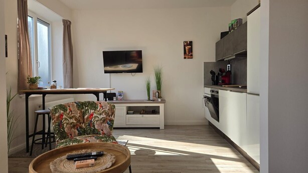 Een moderne keuken met een eethoek, een aan de muur bevestigde televisie en een houten salontafel met afstandsbedieningen.