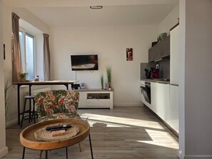 Een moderne keuken met een eethoek, een aan de muur bevestigde televisie en een houten salontafel met afstandsbedieningen.