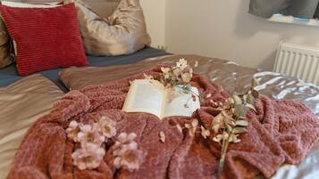 A bed with a red blanket, pillows, and an open book with flowers on it.