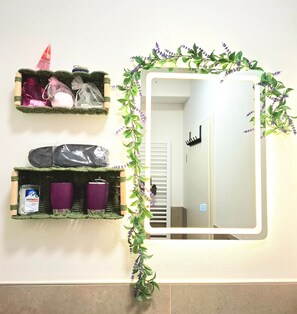 Une salle de bain avec un miroir, deux étagères contenant des articles de toilette et une plante décorative.