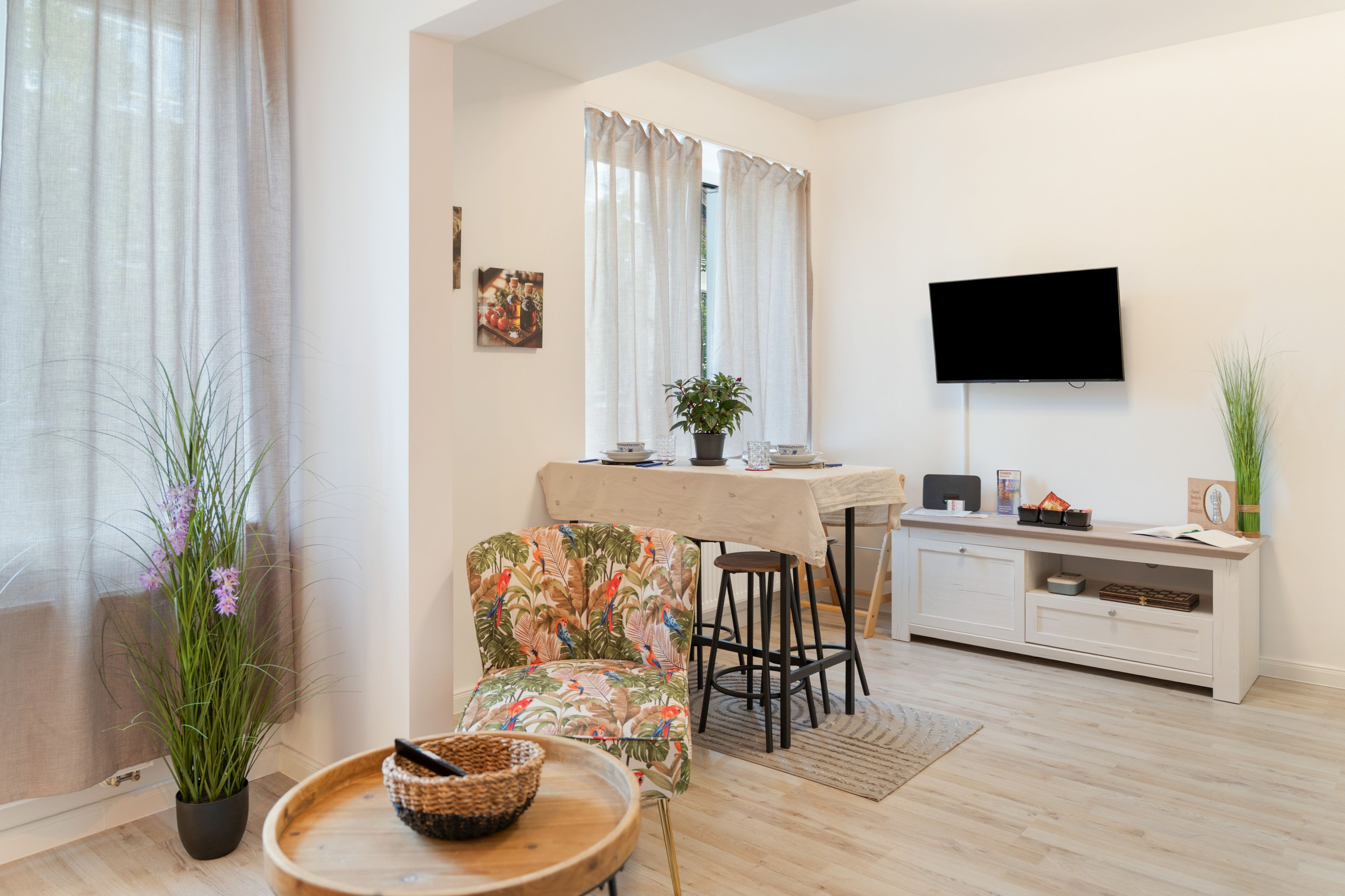 Una sala de estar moderna con comedor, un televisor de pantalla plana montado en la pared y una planta en maceta en el suelo.