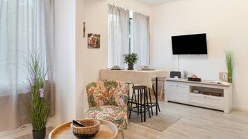 Una sala de estar moderna con comedor, un televisor de pantalla plana montado en la pared y una planta en maceta en el suelo.