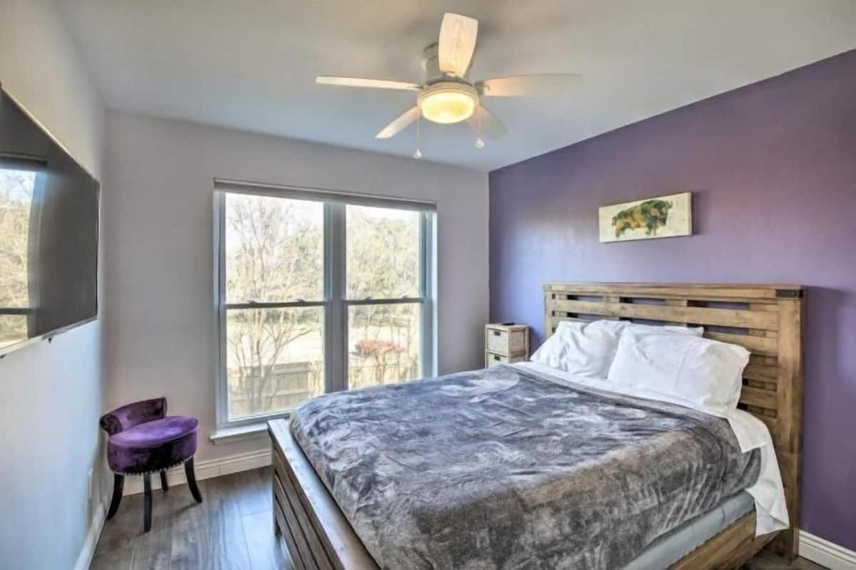 Un dormitorio con cama, ventilador de techo, ventana y una silla.
