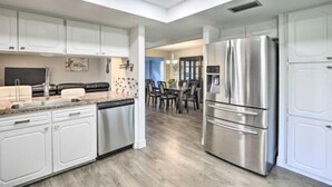 A modern kitchen with white cabinetry, a stainless steel refrigerator, and a dining area with a table and chairs. - Justin Richardson Home w/ Outdoor Oasis & Movie Room (Richardson)