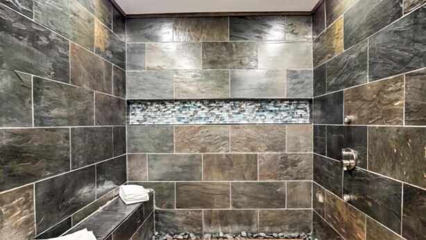 A bathroom with dark stone tiles, a wooden bench, and a mosaic tile accent. - Justin Richardson Home w/ Outdoor Oasis & Movie Room (Richardson)