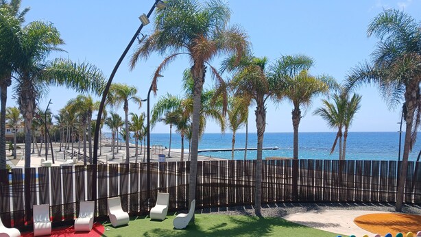 A beachside playground with palm trees, a wooden fence, and a view of the sea. - Vacation Home 'Holiday Esquinita' with Wi-Fi and Air Conditioning (San Bartolomé de Tirajana)